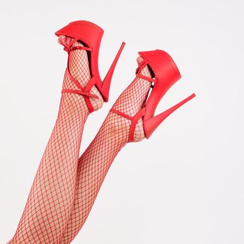 Sexy female legs in high heel red striptease shoes and fishnet stockings. - image