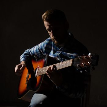 portrait of a man in a plaid shirt plays a fusion of electro-acoustic guitar. Low key portrait.