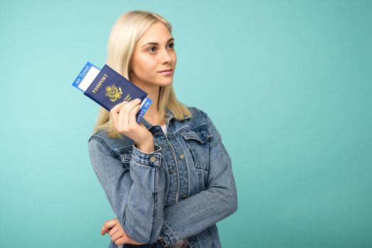 Dreamy girl in a denim jacket holds a passport with airline tickets - image