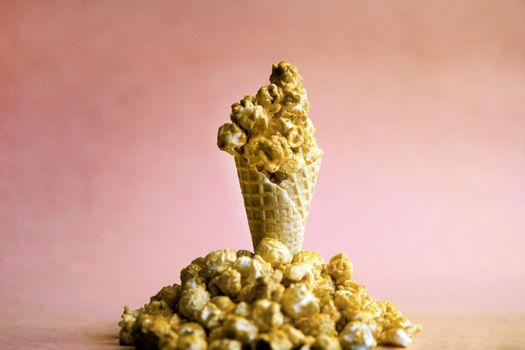 Popcorn spill out from waffle ice cream cone on pastel colorful background. Blue and caramel Popcorn on a cone cornucopia Top view bright hipster background.
