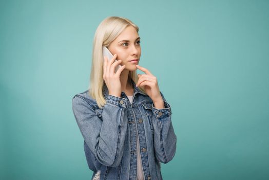 Pensive blonde girl speaks on smartphone isolated on blue background- image