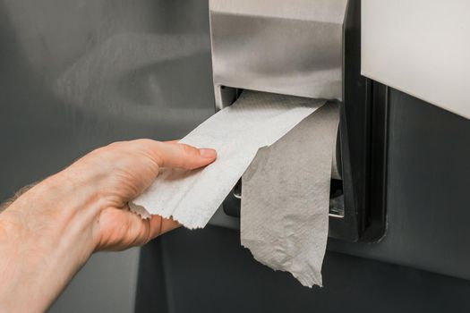 Man's hand takes or tears off toilet paper in a roll, close-up, soft focus.
