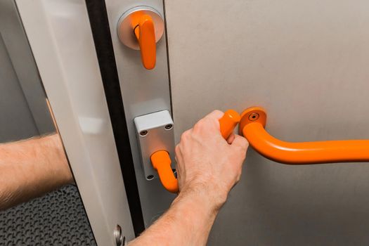 A man's hand holds on to a metal handle next to a handrail and opens a door in a modern electric train.