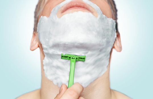 Man with foam on his face is shaving with green razor
