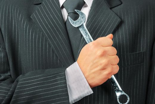 Businessman in a suit holds metal wrench, concept of business creation
