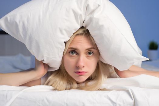 Female lying on bed and closing her ears with pillow - image