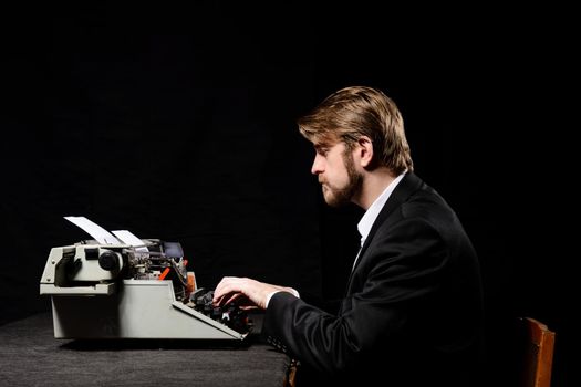 writer, a man in a black jacket typing on typewriter on a black background