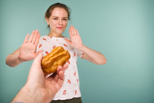 Portrait of pimply teen girl hows hands stop on a delicious cake on blue background