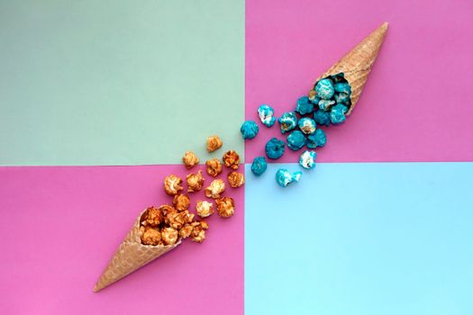 Popcorn spill out from waffle ice cream cone on pastel colorful background. Blue and caramel Popcorn on a cone cornucopia Top view bright hipster background.