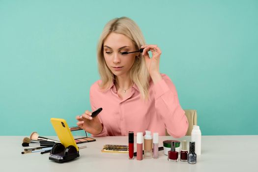 Candid shot of cute young Caucasian woman blogger presenting beauty products and broadcasting live video to social network, using mascara while recording everyday make up tutorial
