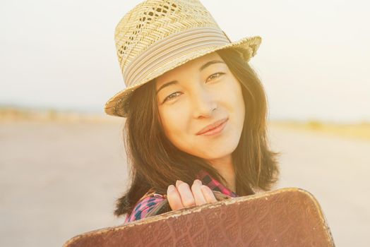 Smiling woman tourist in hat with small vintage suitcase