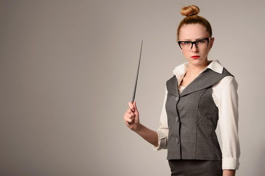 Portrait of young teacher holding pointer. Slim girl in a suit near the white wall