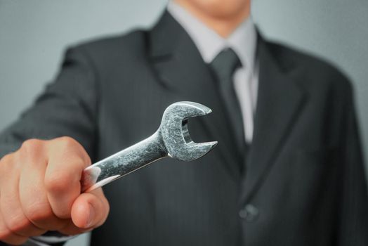 Businessman in a suit holds wrench, focus on wrench, concept of business creation