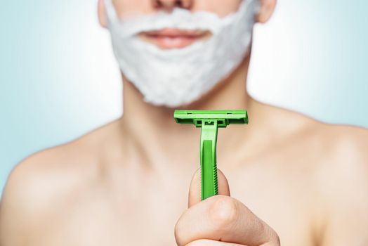 Man with foam on his face holds green razor