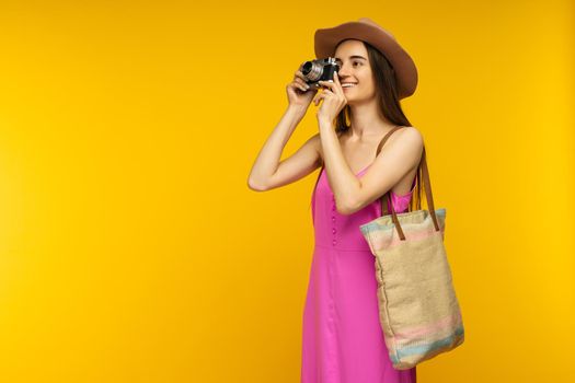 Happy girl in a pink dress and sunglasses holding camera on a yellow background- image