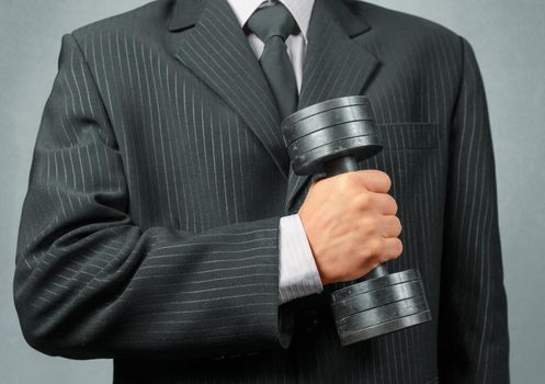 Unrecognizable businessman in a suit holds metal dumbbell, concept of strong business