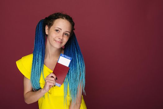 A modern trendy smiling woman in yellow dress with air tickets and a passport in her hand. Young dreamy girl looks at camera. Travel concept