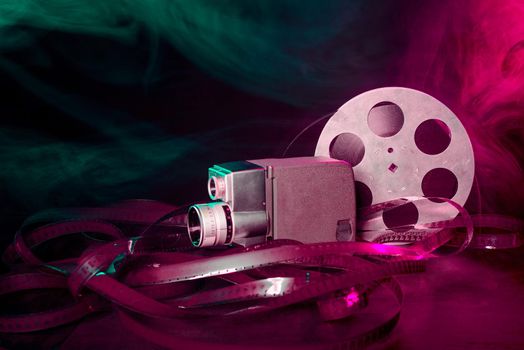 8 mm movie camera with a reel of film in green and purple smoke. dark background
