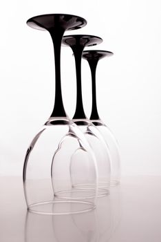 Closeup of three transparent clear crystal empty wine glasses standing close to each other in row isolated on chromium white and grey background, vertical picture