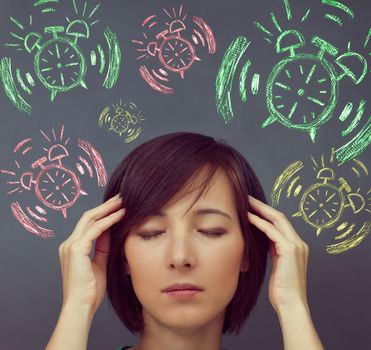 Young woman touches her head on background of alarm clock, concept of time