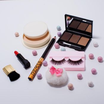 Set of decorative cosmetics false eyelashes, powder, lipstick ,eye shadow white background. Top view of essentials for modern young woman.