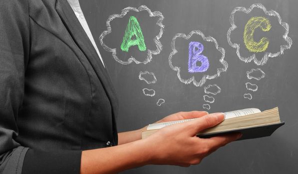 Teacher woman in suit reads a book near a blackboard, ABC alphabet