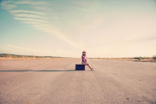 Happy hipster girl sits on vintage suitcase on road, space for text
