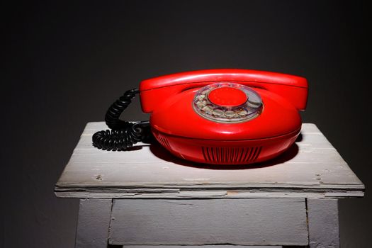 Old red vintage phone on a white chair stool.