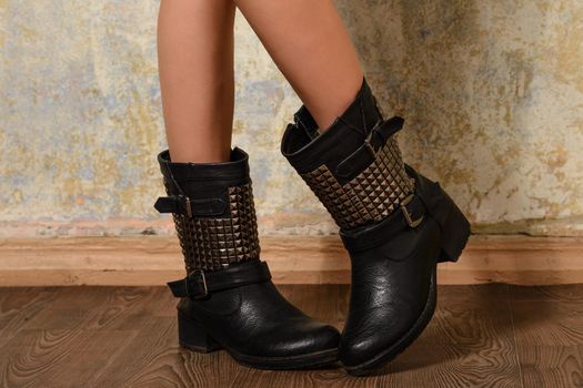 autumn black women&#39;s boots in the straps and rivets dressed the girl standing on the wooden floor near the wall