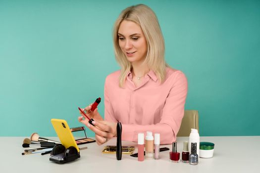 Candid shot of cute young Caucasian woman blogger presenting beauty products and broadcasting live video to social network, using lip gloss while recording everyday make up tutorial
