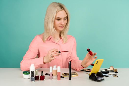 Candid shot of cute young Caucasian woman blogger presenting beauty products and broadcasting live video to social network, using lip gloss while recording everyday make up tutorial