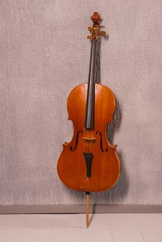 old battered cello standing near a gray textured wall.