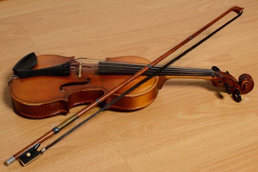 Old violin with a bow lies on a wooden bench