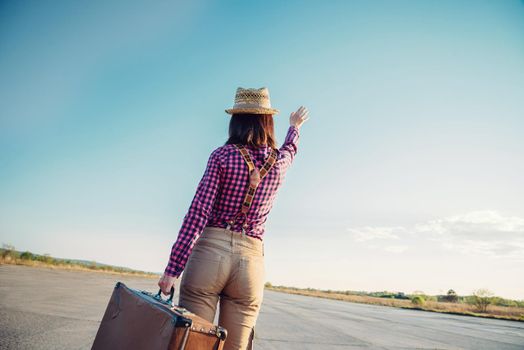 Traveler hipster woman with vintage suitcase waves her hand away, rear view, theme of travel, space for text