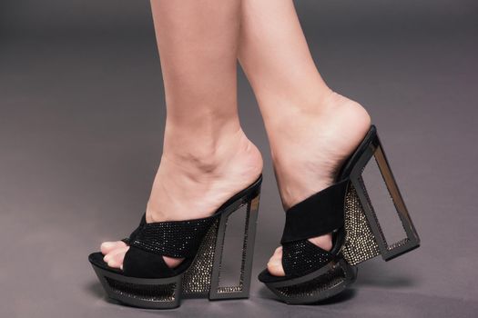 Fashionable woman slender legs in tights black stylish high heels shoes with rhinestones on background