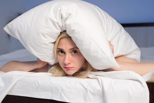 Female lying on bed and closing her ears with pillow - image