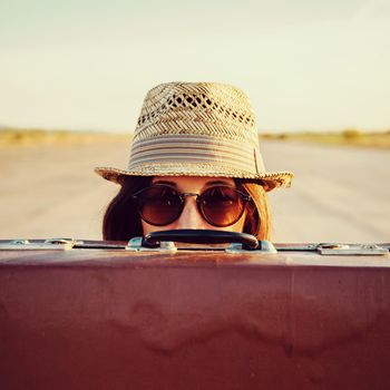 Hipster woman in hat and glasses looks out from vintage suitcase
