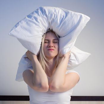 Young woman covering ears with pillow because of noise. - image