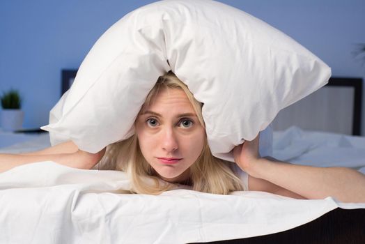 Female lying on bed and closing her ears with pillow - image