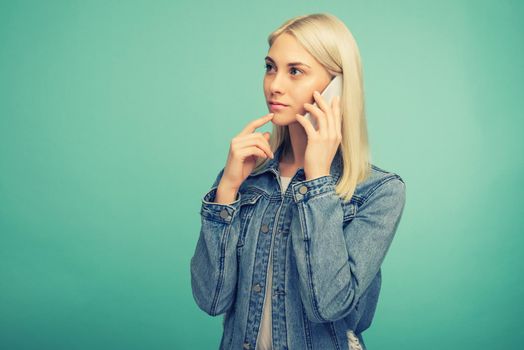 Pensive blonde girl speaks on smartphone isolated on blue background- image toned