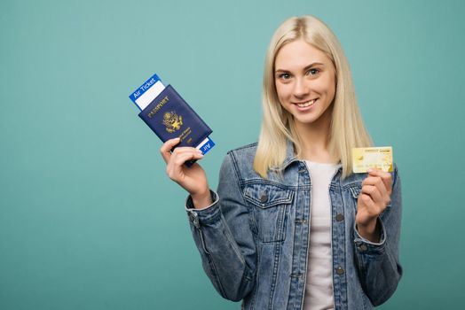 Portrait of a cheerful cute american girl traveller showing passport with air tickets and credit card isolated over blue background