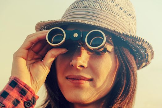 Young traveler woman in hat looks through binoculars