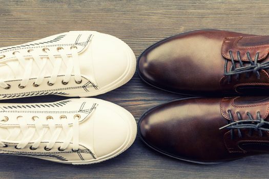 Men's classic brown shoes and white sneakers on a wooden background. Top view - image