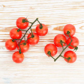 Ripe cherry tomatoes on a twig on a white woden background close up - image