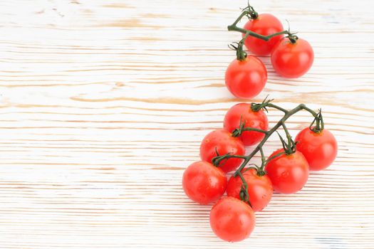 Ripe cherry tomatoes on a twig on a white woden background close up - image