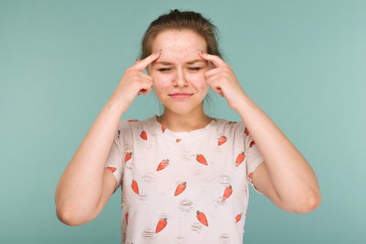 Portrait of teen girl touching her face and looking for acne on blue background