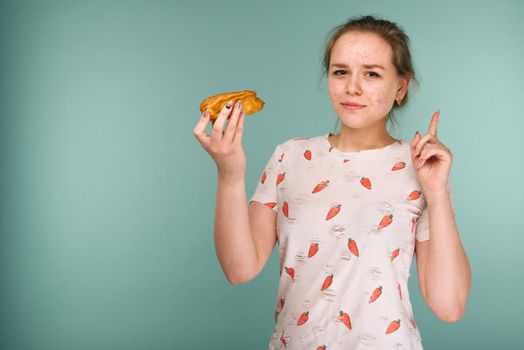Portrait of pimply teen girl wants to eat eclair cake on blue background
