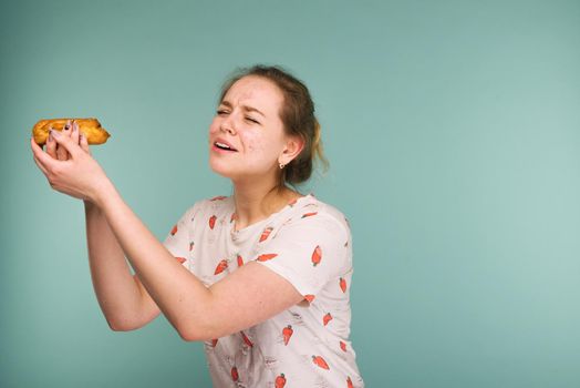 Portrait of pimply teen girl wants to eat eclair cake on blue background