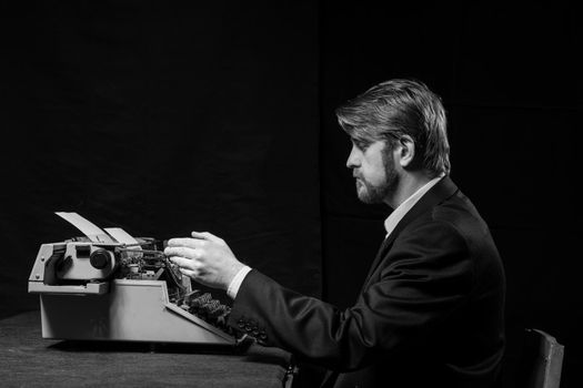 writer, a man in a black jacket typing on typewriter on a black background
