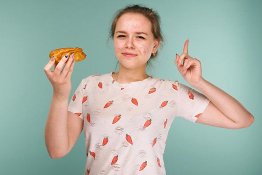 Portrait of pimply teen girl wants to eat eclair cake on blue background